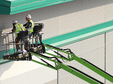 Two men on a giant forklift working on the exterior of a building