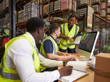 Three people in safety vests at a computer in a warehouse Three people in safety vests at a computer in a warehouse